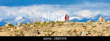 Atemberaubendes Panorama des Tibetischen Hochlandes mit schneebedeckten Bergen. Pilger mit roter Robe im Vordergrund. Stockfoto