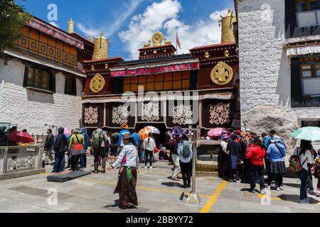 Besucher - sowohl Pilger als auch Touristen vor dem Jokhang-Tempel. Einer der Touristenmagneten von Tibets. Detail: Chinesische Flagge neben dem goldenen Dharma-Rad. Stockfoto