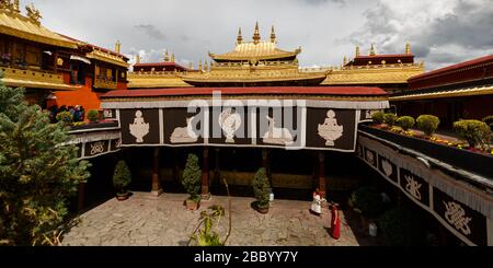 Panorama-Blick auf Dach und Hof mit Mönchen des Jokhang-Tempels (UNESCO-Weltkulturerbe). Die wichtigsten Dacheigenschaften: Dharma-Rad und Hirte. Stockfoto