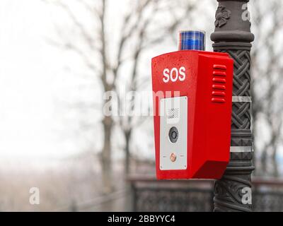 Hilfe- oder Polizeiruftaste. SOS. Auf der Straße, auf einem Lampenpfosten, ist ein Ständer mit einem Knopf befestigt. Rotes Gehäuse mit blauer Warnleuchte oben. Stockfoto