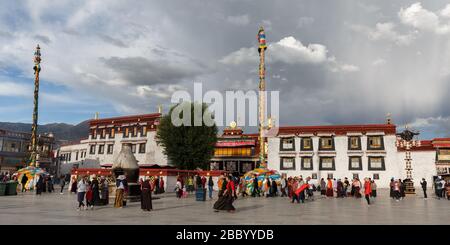 Jokhang Tempel unter einem wolkigen Himmel. Panoramablick auf das UNESCO-Weltkulturerbe mit goldenem Dharma-Rad. Im Vordergrund Pilger. Stockfoto