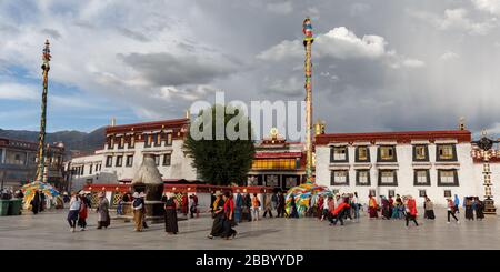 Panoramablick auf den Jokhang Tempel. Im Vordergrund der Hauptplatz mit Pilgern und Touristen. Wolkiger Himmel über dem UNESCO-Weltkulturerbe. Stockfoto