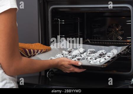 Der Backvorgang von Brownie-Plätzchen. Das Foto zeigt weibliche Hände, setzt Plätzchen in den Ofen. Stockfoto