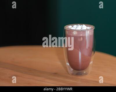 Kakao mit Marshmallows in einem Glas. Vor dem Hintergrund eines Tisches und einer dunkelgrünen Wand. Stockfoto