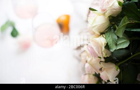 Blumenstrauß aus weißen Rosen und Wein. Nahblüten und verschwommene Weingläser ohne Fokus. Freier Speicherplatz für Text. Weicher Fokus. Kopierbereich Stockfoto