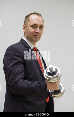 Porträt eines selbstbewussten Geschäftsmannes, der die Hanteln über den hellen Hintergrund hebt. Stockfoto