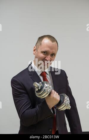 Porträt eines selbstbewussten Geschäftsmannes, der die Hanteln über den hellen Hintergrund hebt. Stockfoto