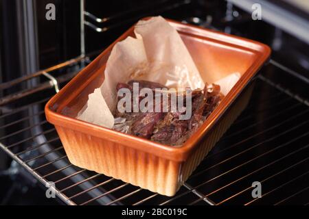 Entenfleisch wird im Ofen auf einem keramischen Backblech gebacken. Nahaufnahme. Stockfoto