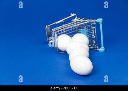 Eier fielen aus dem Warenkorb. Hühnereier in einem Einkaufswagen. Isoliert auf Blau Stockfoto