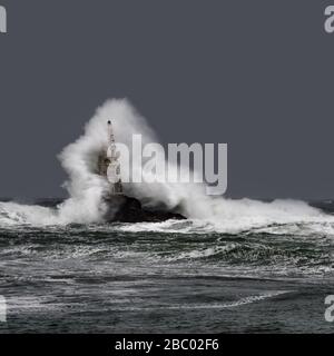 Große Welle gegen den alten Leuchtturm im Hafen von Ahtopol, Schwarzes Meer, Bulgarien an einem stürmischen Tag. Gefahr, dramatische Szene. Stockfoto