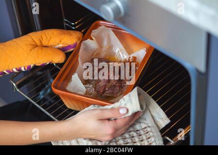 Das Entenfleisch wird im Ofen auf einem keramischen Backblech gebacken. Die Hände eines Mädchens legen das Backen in den Ofen. Stockfoto