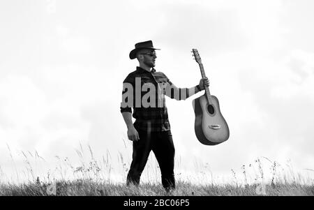 Country Music Konzept. Gitarrist Country Sänger steht im Hintergrund von Field Sky. Landhausstil. Sommerurlaub. Wanderlied. Inspirierter Country-Musiker. Vereint mit der Natur. Gutaussehender Mann mit Gitarre. Stockfoto