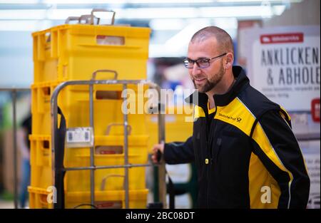 Gangelt Birgden, Deutschland. April 2020. Michael Peltzer, Postbote in Gangelt, fährt Lebensmittel in Briefkästen durch den Supermarkt im Rewe-Supermarkt in Schmiz. Im Kreis Heinsberg, der besonders vom Coronavirus betroffen ist, startet die Deutsche Post ein Pilotprojekt zur Bereitstellung grundlegender Dienstleistungen für Risikogruppen, die von der Post mit Lebensmitteln und Haushaltswaren aus dem lokalen Einzelhandel versorgt werden können. Credit: Jonas-Güttler / dpa / Alamy Live News Stockfoto