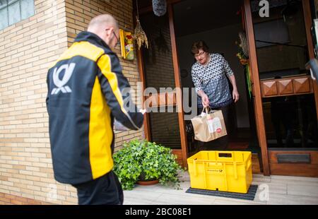 Gangelt Birgden, Deutschland. April 2020. Michael Peltzer (l), Postbote in Gangelt, führt Lebensmittel in Briefkästen zu einem Quarantänebewohner. Im Kreis Heinsberg, der besonders vom Coronavirus betroffen ist, startet die Deutsche Post ein Pilotprojekt zur Bereitstellung von Grundleistungen für Risikogruppen, die von der Deutschen Post mit Lebensmitteln und Haushaltswaren des örtlichen Einzelhandels versorgt werden können. Credit: Jonas-Güttler / dpa / Alamy Live News Stockfoto