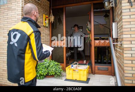 Gangelt Birgden, Deutschland. April 2020. Michael Peltzer (l), Postbote in Gangelt, führt Lebensmittel in Briefkästen zu einem Quarantänebewohner. Im Kreis Heinsberg, der besonders vom Coronavirus betroffen ist, startet die Deutsche Post ein Pilotprojekt zur Bereitstellung von Grundleistungen für Risikogruppen, die von der Deutschen Post mit Lebensmitteln und Haushaltswaren des örtlichen Einzelhandels versorgt werden können. Credit: Jonas-Güttler / dpa / Alamy Live News Stockfoto
