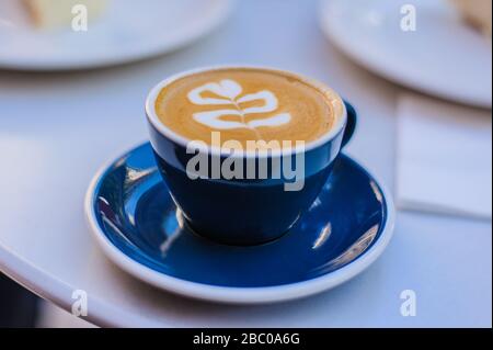 Aromatischer Kaffee-Cappuccino in einer blauen Tasse auf einer Untertasse steht auf einem weißen Tisch Stockfoto