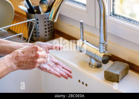 Nahaufnahme der Hände einer Frau, die ihre Hände gründlich mit Seife unter dem Hahn der Küchenspüle waschen. Stockfoto