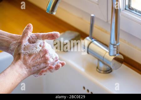 Nahaufnahme der Hände einer Frau, die ihre Hände gründlich mit Seife unter dem Hahn der Küchenspüle waschen. Stockfoto