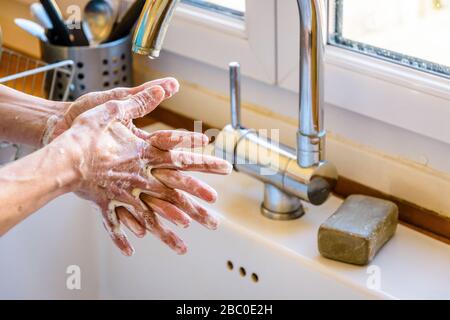 Nahaufnahme der Hände einer Frau, die ihre Hände gründlich mit Seife unter dem Hahn der Küchenspüle waschen. Stockfoto