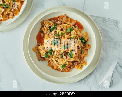 Nudelfarfalle mit Tomatensauce und gemahlenem Fleisch auf dem Tisch aus weißem Marmor. Idee und Rezepte für einfaches, einfaches Mittagessen oder Abendessen, eintopfige Fleischgulasch. Draufsicht oder flache Lage Stockfoto