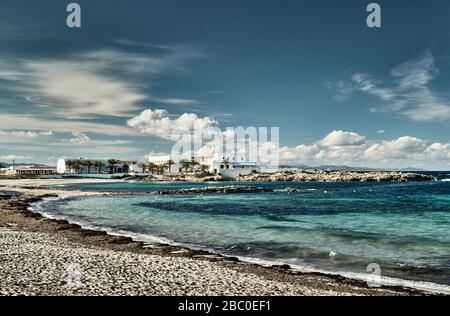 Die Landschaft des balearen Meeres und die unwahrscheinliche Schönheitsbucht, das azurblaue Wasser, der Himmel mit Wolken, einsame Gebäude liegen im Hintergrund, Strand ohne Menschen Stockfoto