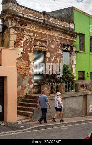 Südafrika, Kapstadt, Schotsche Knoof, Bo Kaap, Chiappini St, Paar, das an einem nicht restaurierten Gebäude vorbeiläuft Stockfoto