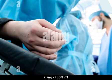 Hand eines Patienten, der auf dem Operationstisch liegt. Der Patient schläft unter Vollnarkose. Im Hintergrund sind Chirurgen in chirurgischer Kleidung a Stockfoto