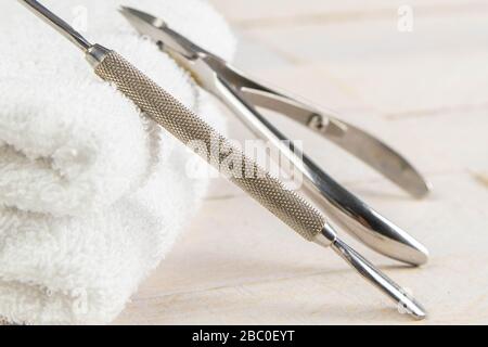 Eine Reihe von kosmetischen Werkzeugen für Maniküre und Pediküre auf blauem Hintergrund. Ein Scheffer und ein Häutchenschneider rappten bis zu einem weißen Handtuch, das auf einem steht Stockfoto