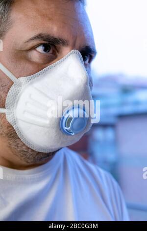Ein Mann mit einer schützenden medizinischen Maske wartet auf das Ende der Kovid-19-Notquarantäne, hinter dem Glas seines Heimatfensters. Stockfoto