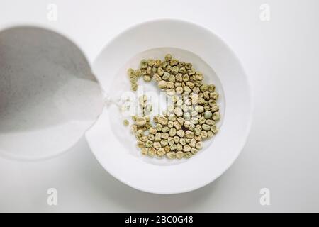 Grüne Erbsen in warmem Wasser in der Schüssel einweichen, um den Keimvorgang beim Pflanzen im Garten zu fixieren. Die Samen weichen in der weißen Schüssel ein. Stockfoto