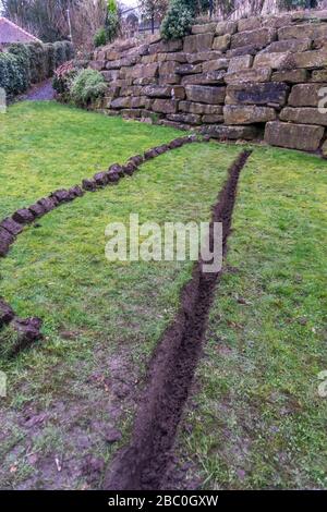 Installation eines Ablaufgrabens in einem Gartenrasen, Stockfoto