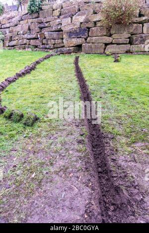 Installation eines Ablaufgrabens in einem Gartenrasen, Stockfoto