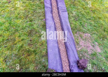 Installation eines Ablaufgrabens in einem Gartenrasen, Stockfoto