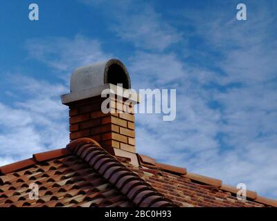 Gemauerte Kamine. Grauer gewölbter Betondeckelstein. Metall blinkend. Rotbraune Terrakotta-Dachziegel und -Schlitze. Blauer Himmel, weiße Wolken. Konstruktion. Stockfoto