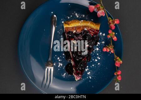 Scheiben von Blaubeeren Mousse mit Spiegelglasur verzierte Beeren und Minzblätter auf einem blauen Teller mit roten Blumen stehen auf schwarzem Tisch, nah oben Stockfoto