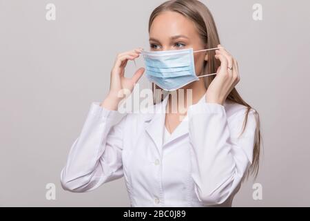 Junge Frau Doktor trägt auf weißem Hintergrund eine Brille und eine weiße Schutzmaske im Gesicht Stockfoto