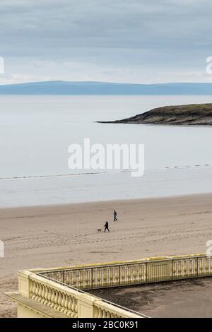 Blick über die Whitmore Bay auf Barry Island in Richtung Exmoor am Horizont. Nur zwei Menschen gehen während der Covid-19-Krisen am Strand. Stockfoto