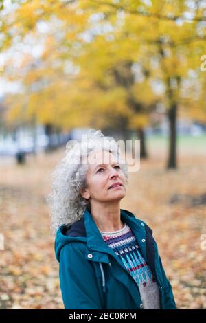 Nachdenkliche Seniorin, die Herbstbäume im Park betrachtet Stockfoto