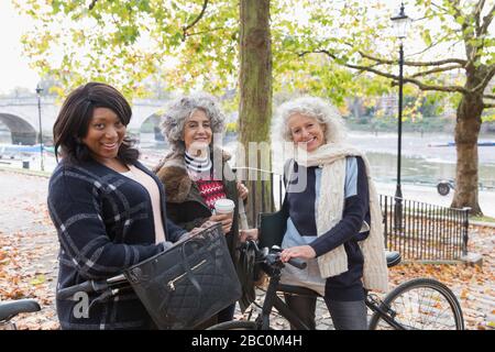 Portrait lächelnd, selbstbewusst aktive Seniorinnen mit Kaffee und Fahrrädern im Herbstpark befreundet Stockfoto
