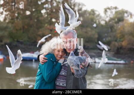 Verspieltes Senioren-Paar füttert Tauben am Teich im Park Stockfoto