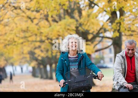 Lächelnde, unbeschwerte Seniorin radelt im Herbstpark unter Bäumen Stockfoto