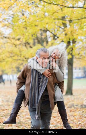 Verspieltes Senioren-Paar piggybacking im Herbstpark Stockfoto