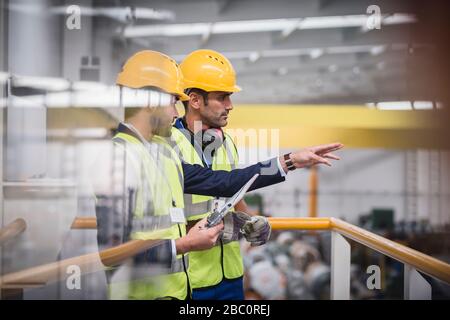 Männliche Vorgesetzte mit Zwischenablage, die auf der Plattform im Werk sprechen Stockfoto