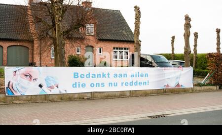 Aaigem, Belgien, 29. März 2020: Banner mit dem Image des medizinischen Personals und vielen Dank an alle, die uns jetzt während der Coronakrise retten. Vor einem Wohnhaus in ländlicher Umgebung. Auf Niederländisch: Bedankt aan allen die ons nu redden. Stockfoto