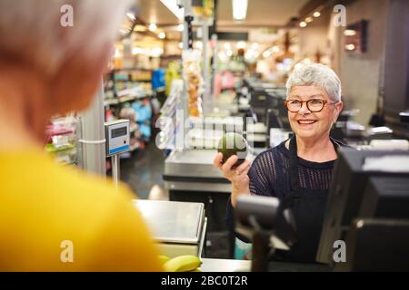 Lächelnde leitende Kassiererin hilft Kunden beim Lebensmittel-Checkout Stockfoto