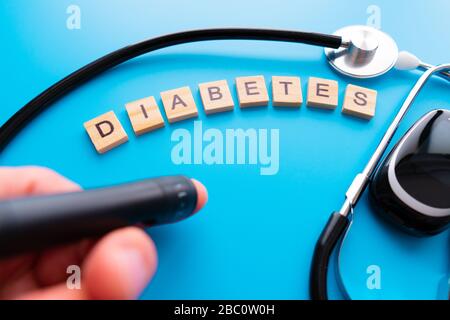 Holztext für Diabetes. Flache Laienzusammensetzung mit Blutzuckermessgerät und Stethoskop auf hellblauem Hintergrund. Leerzeichen für Text Stockfoto