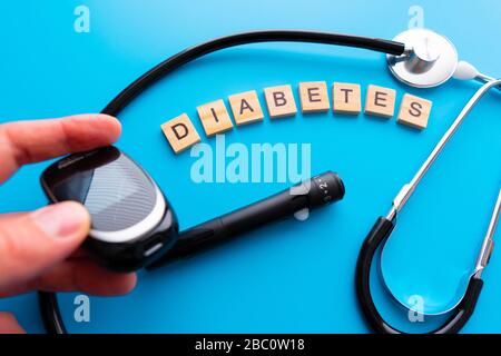 Holztext für Diabetes. Flache Laienzusammensetzung mit Blutzuckermessgerät und Stethoskop auf hellblauem Hintergrund. Leerzeichen für Text Stockfoto