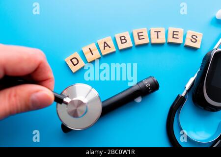 Holztext für Diabetes. Flache Laienzusammensetzung mit Blutzuckermessgerät und Stethoskop auf hellblauem Hintergrund. Leerzeichen für Text Stockfoto