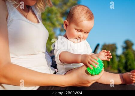 Muttertag. Baby Mädchen, die mit Spielzeug spielen, das auf den Knien ihrer Mutter im Sommerpark sitzt. Familie hat Spaß im Freien Stockfoto