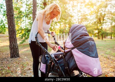 Muttertag. Junge Mutter, die im Sommerpark spazieren geht und mit dem Kinderwagen Spielzeug schenkt. Frau verbringt Zeit mit Kind Stockfoto
